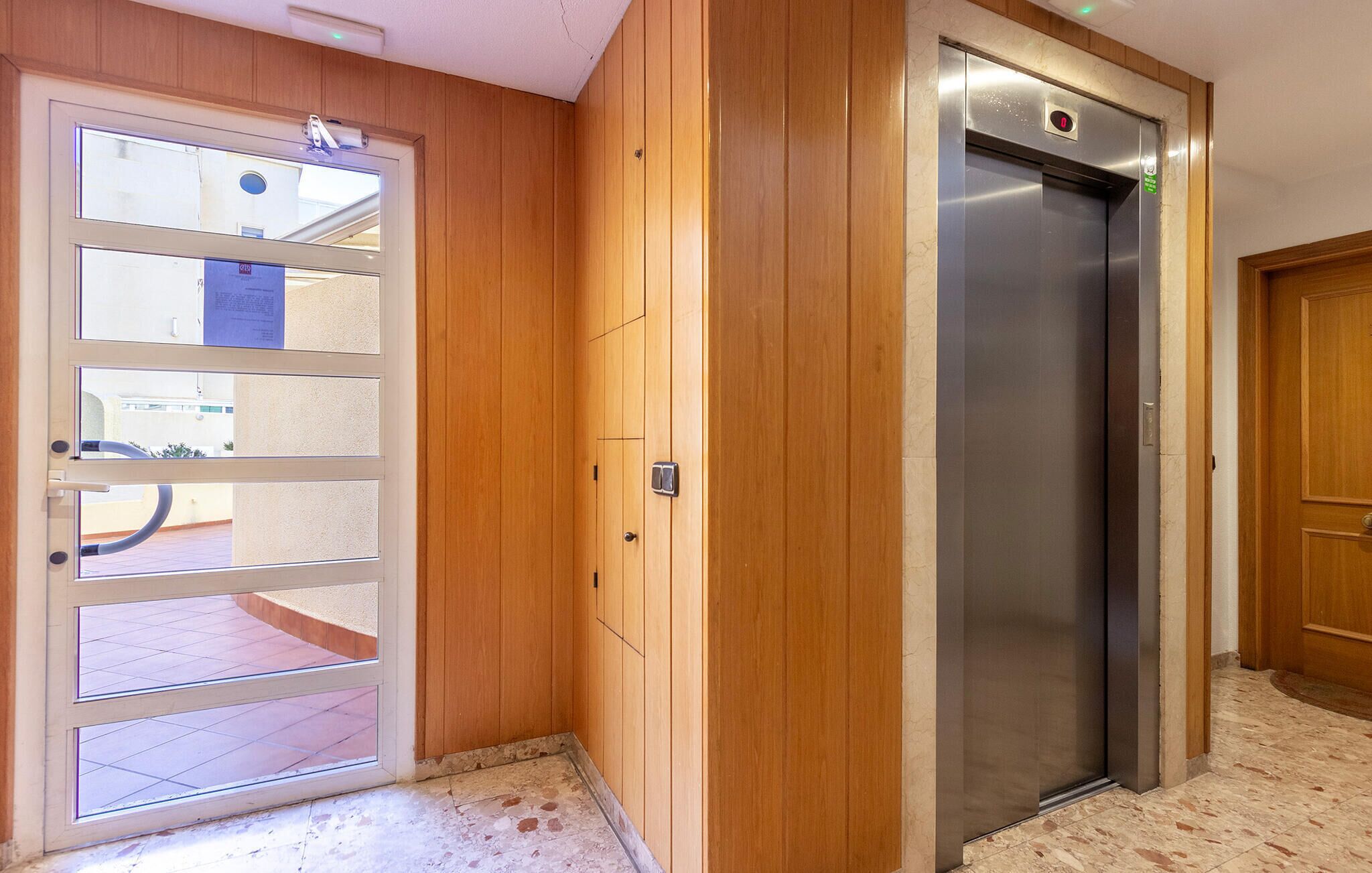 Un ascenseur moderne doté d’un écran numérique, de parois en lambris de bois et d’une porte en verre à plusieurs vitres.