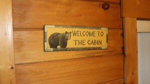 Una cabaña de madera con un letrero de bienvenida que muestra una ilustración de un oso.