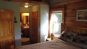 Un dormitorio con cabecera de madera, cama con colcha, mesita de noche con lámpara y ventana con vistas al exterior.
