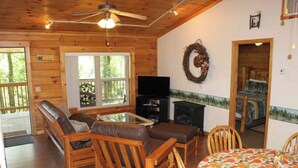 Interior acogedor de una cabaña con techo de madera, chimenea, televisor y comedor.