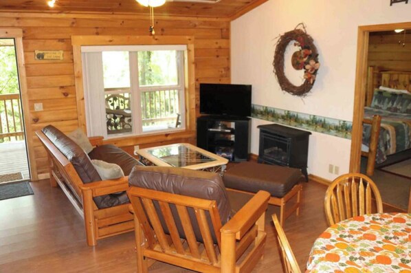 A wooden cabin interior with a sofa, chairs, a table, a fireplace, and a television.