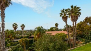 Un jardin luxuriant, parsemé de palmiers, un bâtiment au toit rouge et un ciel d’un bleu limpide.