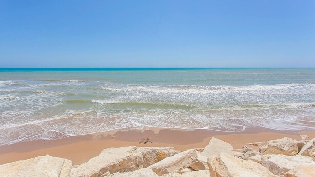 Une plage avec une eau d’un bleu limpide et un rivage sablonneux.