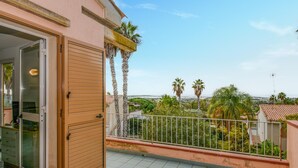 Un balcon offrant une vue sur des palmiers et un paysage lointain.