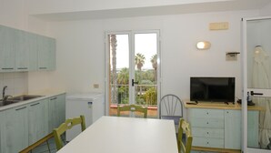 Une cuisine compacte avec un coin repas, un téléviseur et un balcon offrant une vue sur les palmiers.
