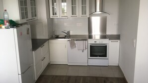 A compact kitchen with white cabinets, a stainless steel range hood, a built-in oven, and a refrigerator.