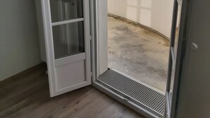 A room with a sliding glass door leading to a balcony. The room has a wooden floor and a white door with a glass panel.