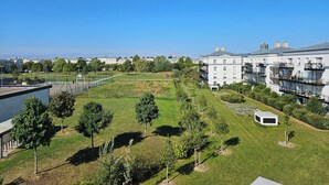 A residential area with a large white building with multiple balconies, a well-maintained lawn, and a sports field in the background.