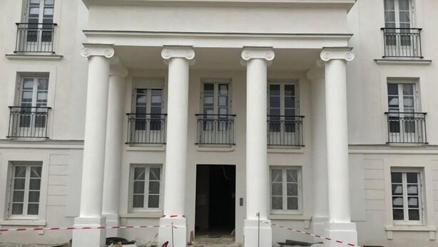 A large, white building with a grand entrance featuring columns and a central doorway.