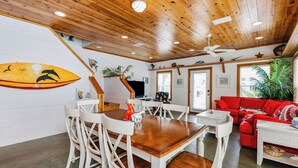 A wooden ceiling with recessed lighting, a dining area with white chairs and a wooden table, a red sofa, and a ceiling fan. - Seashell Escape--3 BR House in Village Walk, Sleeps 10, Near Beach, Dogs OK! (Port Aransas)