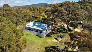 Une maison moderne dotée d’une grande terrasse, entourée d’une forêt dense et avec des collines en arrière-plan.