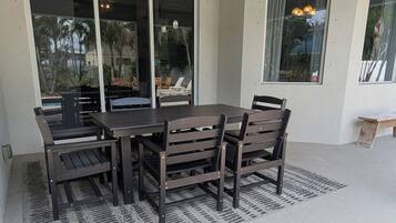 Eine Terrasse im Freien mit Tisch und Stühlen, einem gemusterten Teppich und Blick durch Glastüren.