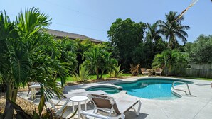 A backyard with a swimming pool, surrounded by palm trees and chairs. - Hibiscus Hideaway in Cocoa Beach (Cocoa Beach)