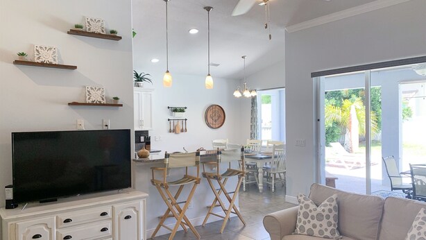 A modern living room with a flat-screen TV, a beige sofa, and a dining area with a table and chairs. - Hibiscus Hideaway in Cocoa Beach (Cocoa Beach)
