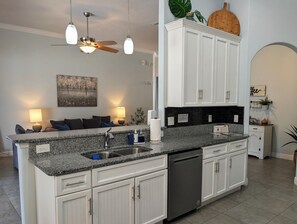 A modern kitchen with granite countertops, white cabinetry, a dishwasher, and pendant lighting. - Hibiscus Hideaway: Pool, Spa & Steps to the beach (Cocoa Beach)