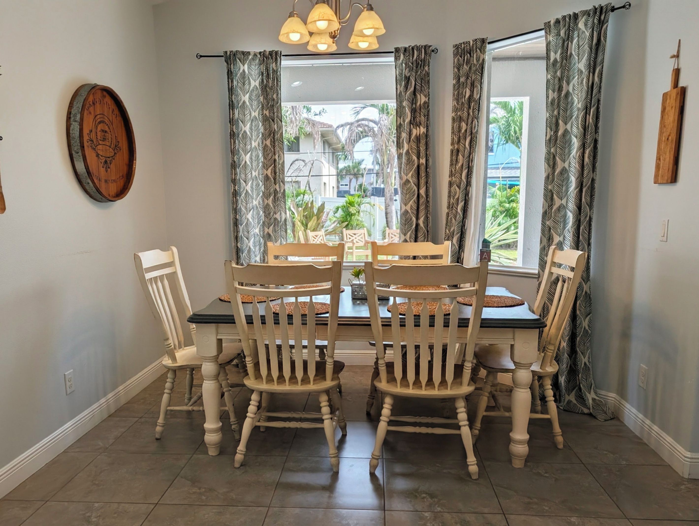 A dining area with a table and four chairs, a wooden wall decor, and a window with patterned curtains.