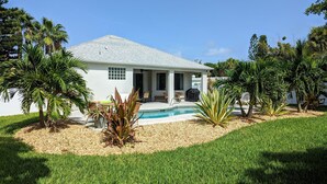 A white house with a pool, surrounded by palm trees and a well-maintained lawn. - Hibiscus Hideaway in Cocoa Beach (Cocoa Beach)