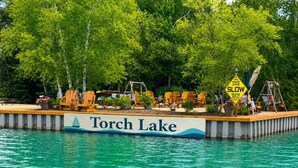 Rantavyöhyke, jossa on kyltti, jossa lukee ”Torch Lake”, puisia tuoleja, keinuteline ja kyltti, jossa lukee ”Hidas vauhti, ei aaltoja”.