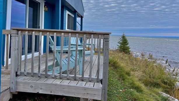 Une maison bleue avec une terrasse en bois donnant sur une étendue d’eau.