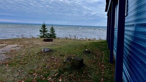 Une vue sur un lac, avec une zone herbeuse et deux arbres au premier plan, et un bâtiment à la façade bleue sur la droite.