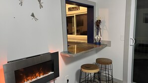 Un salon moderne doté d’une cheminée intégrée, d’un coin bar avec des tabourets et d’un élément décoratif mural.