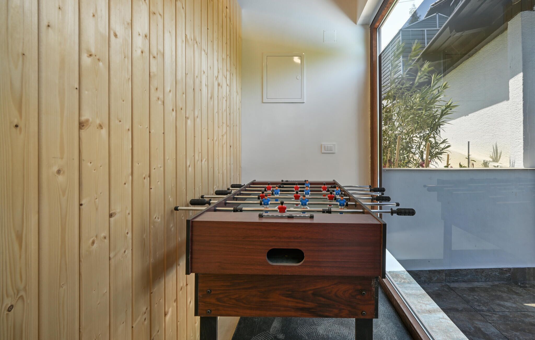 A foosball table in a room with wooden walls and a window overlooking a garden.