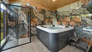 Ein modernes Badezimmer mit Duschkabine aus Glas, Whirlpool und einer Wand aus Naturstein.