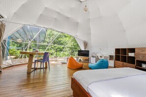 Een ruime kamer met een groot bed, een houten tafel, een televisie en uitzicht door een groot raam.