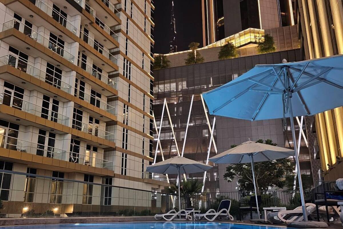 A swimming pool with lounge chairs and umbrellas, surrounded by high-rise buildings at night.
