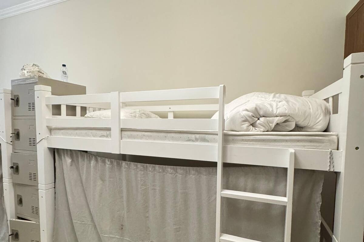 A bunk bed with a ladder, a curtain, and a water bottle on the top bunk.
