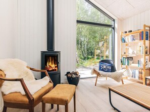 A cozy room with a wood-burning stove, a leather chair, a wooden bench, and a bookshelf filled with books. - 5 Star Holiday Home in Laeso (Læsø)