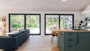 Cozinha moderna com ilha de madeira, área de jantar com mesa e cadeiras, sofá e estante de livros.