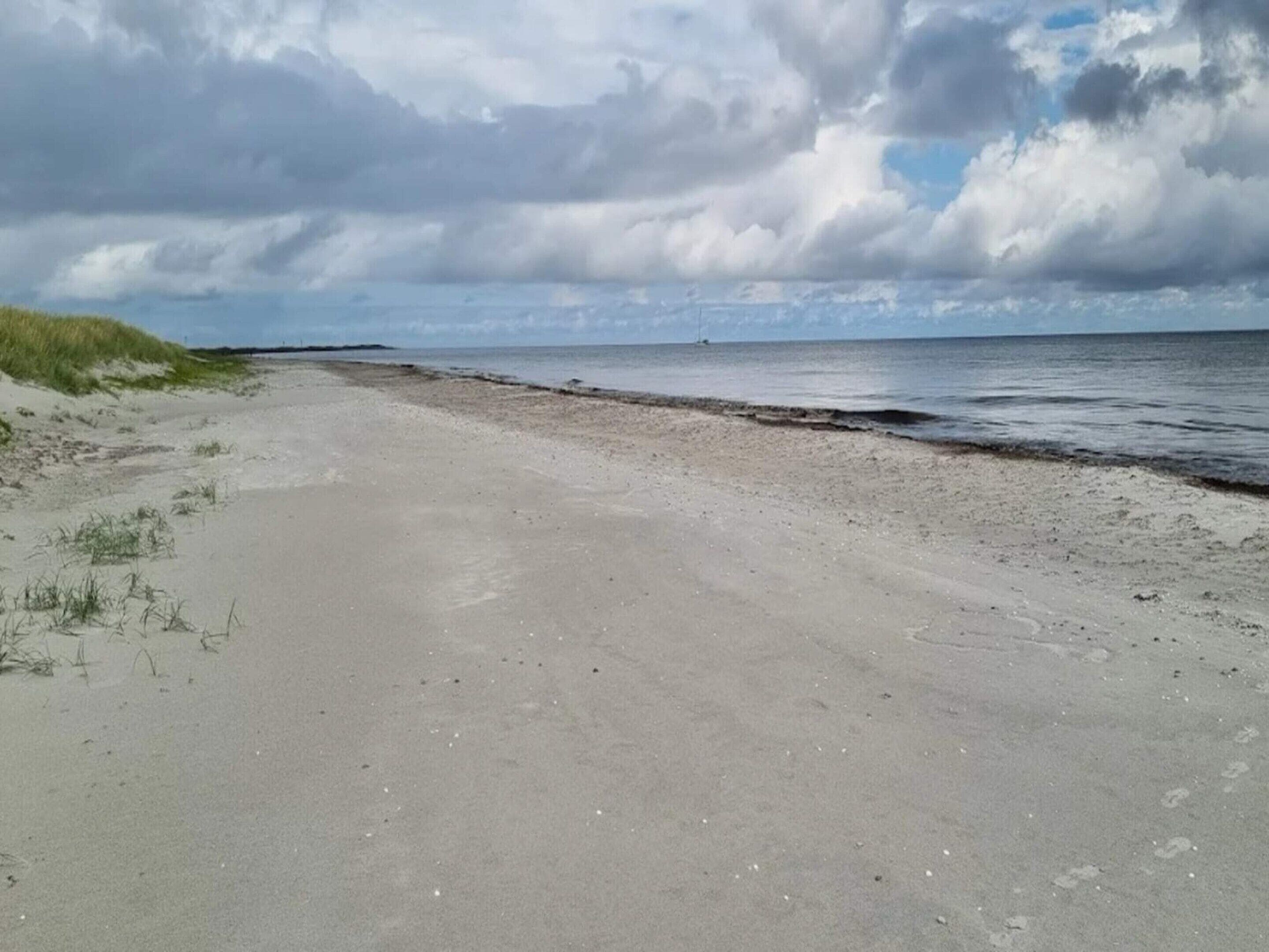 A beach with sand, grass, and a cloudy sky.