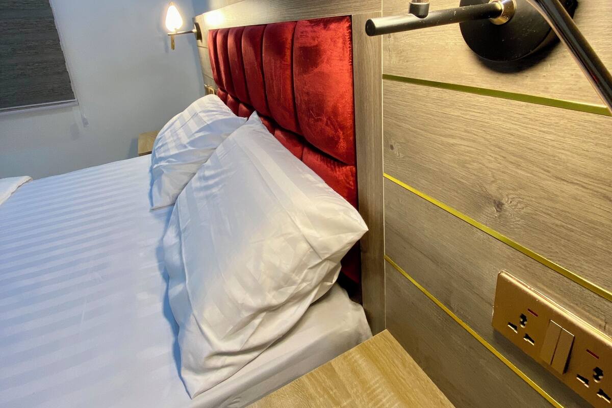 Ein Hotelzimmer mit Bett, rotem Kopfteil, Wandlampe und Klimaanlage.