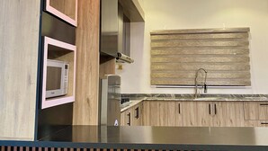 A modern kitchen with a built-in microwave, stainless steel appliances, and a wooden backsplash. - BA2 Homes (Abuja)