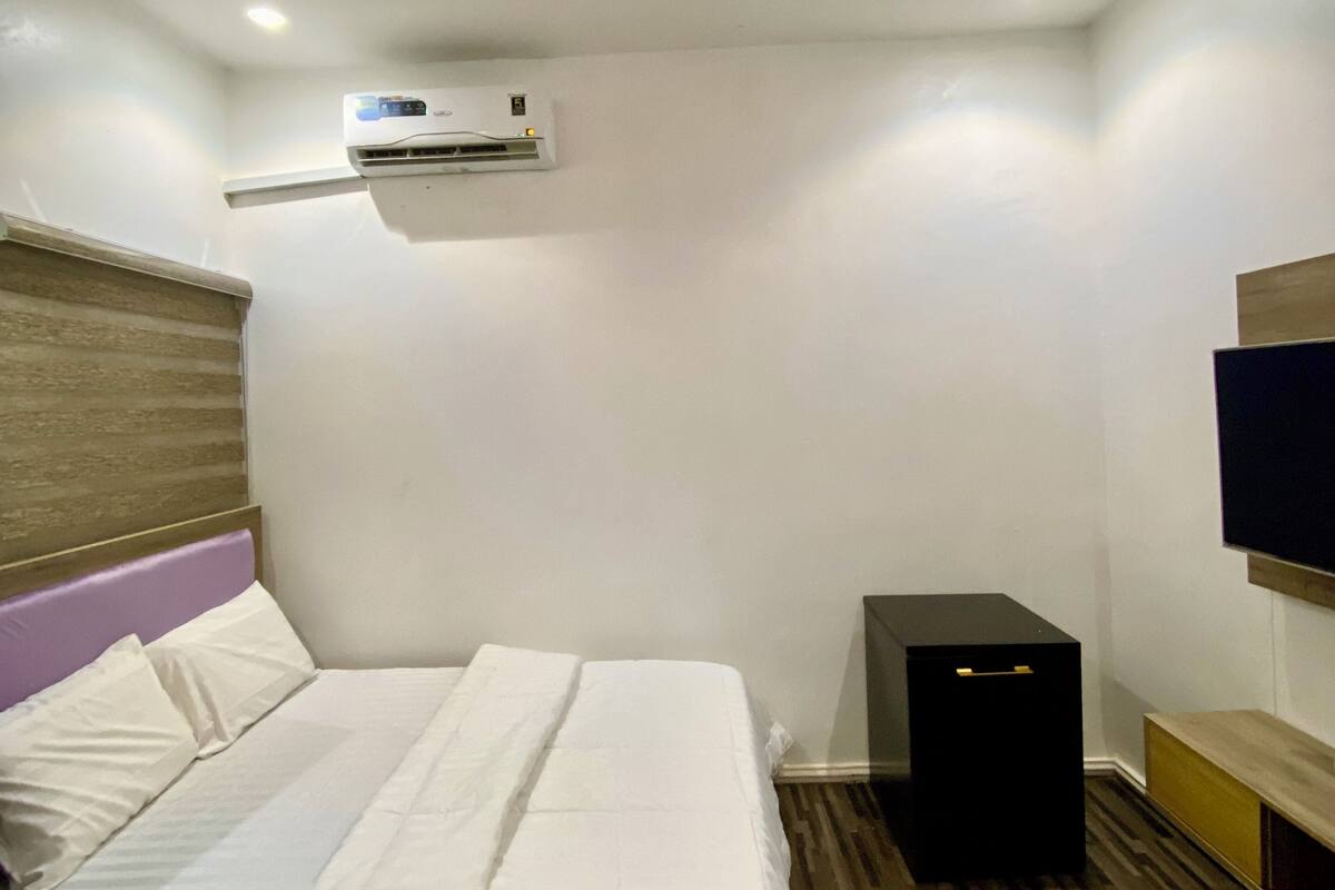 Ein Hotelzimmer mit Bett, Klimaanlage, Fernseher und Holzboden.