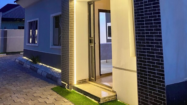 A modern house with a well-lit entrance, paved driveway, and a small lawn area. - BA2 Homes (Abuja)