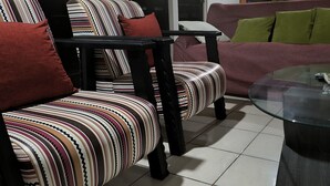 Uma sala de estar com poltronas listradas, uma mesa de centro de vidro e um sofá com almofadas verdes e brancas.