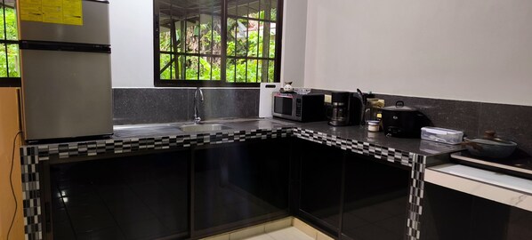 Una cocina moderna con un salpicadero de azulejos blanco y negro, un refrigerador de acero inoxidable, un microondas, una cafetera y una ventana con vistas a zonas verdes.