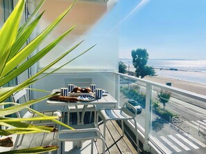 Un balcón con una mesa lista para el desayuno, vista a la playa y una calle con coches.