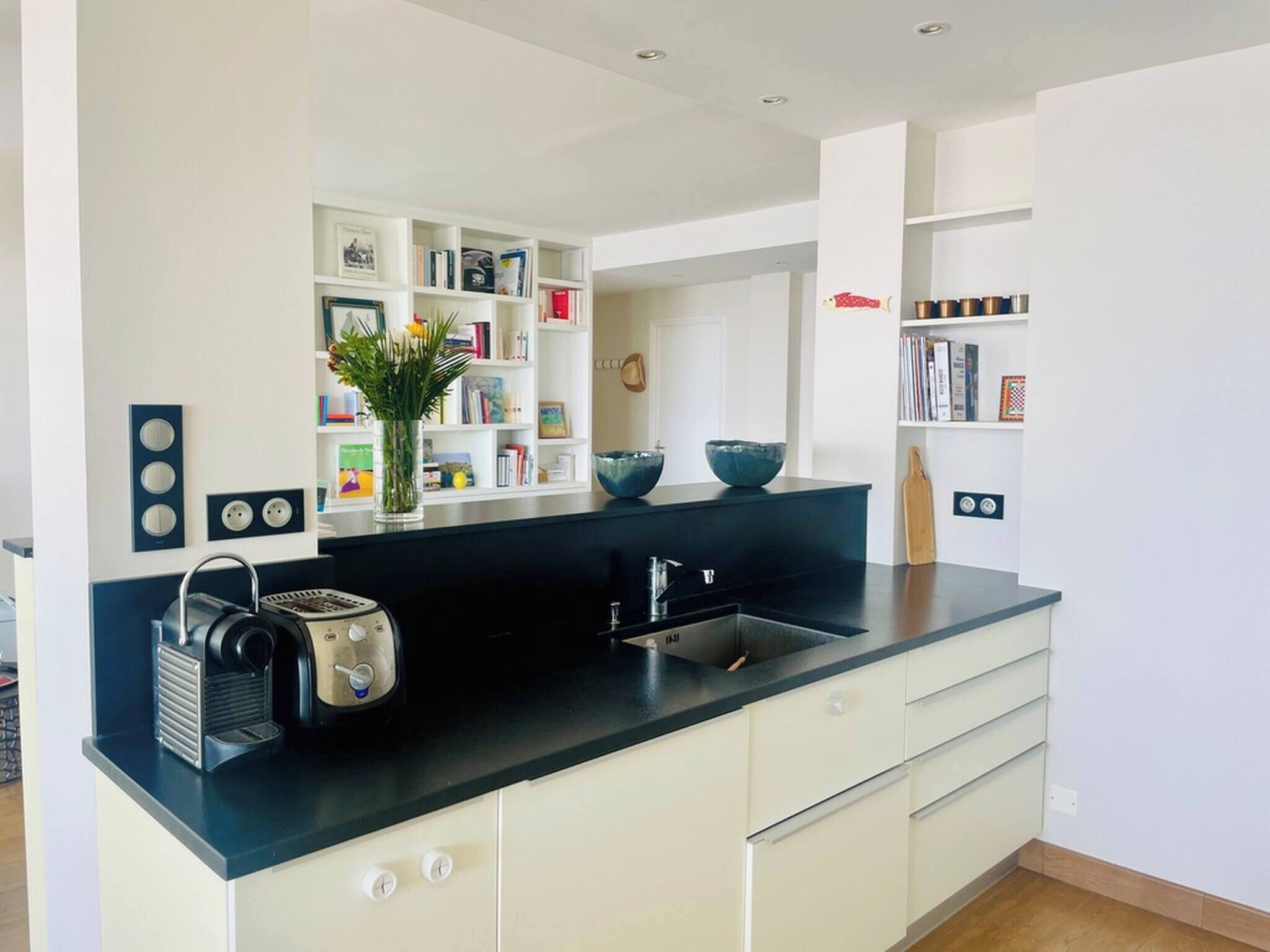 A modern kitchen with a black countertop, white cabinetry, and a built-in bookshelf.