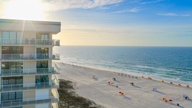 Un hotel frente a la playa con varios balcones, una playa de arena y vista al océano.