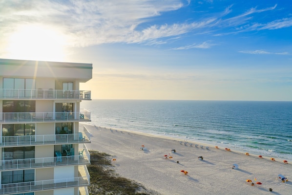 A beachfront hotel with multiple balconies, a sandy beach, and a view of the ocean.