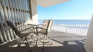 Un balcón con una mesa y sillas, vista a la playa y una barandilla.