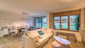 A cozy living room with a sofa, a dining table, and chairs. There is a window with a view of the outdoors. - Appartement Sérénité - Welkeys (Chamonix-Mont-Blanc)