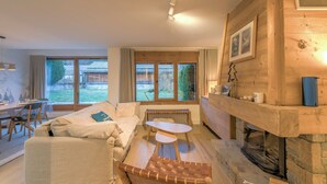 A cozy living room with a sofa, a small table, and a fireplace. There is a window with a view of the outdoors. - Appartement Sérénité - Welkeys (Chamonix-Mont-Blanc)
