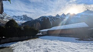 A snow-covered landscape with mountains in the background and a building with a snow-covered roof. - Appartement Sérénité - Welkeys (Chamonix-Mont-Blanc)