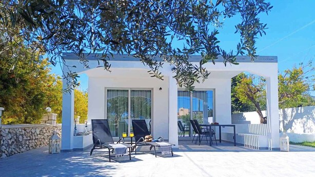 Un patio moderno al aire libre con una estructura blanca, sillones de descanso negros y una mesa.