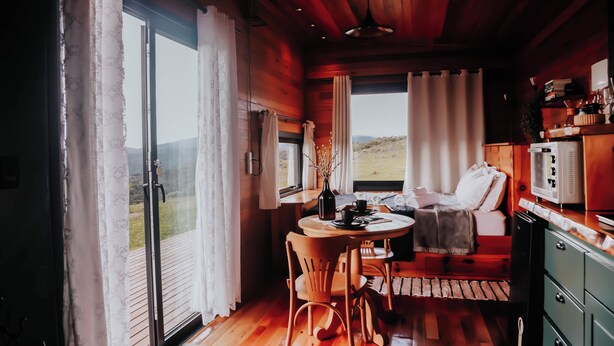 A cozy cabin interior with a dining area, a bed, and a kitchenette.