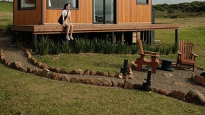 A modern wooden cabin with large windows, a deck, and outdoor seating.